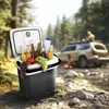 A portable cooler filled with drinks and fruit is placed on the ground next to a stream, with a car and people in the background. Anteprima dell’immagine prodotto