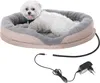 A small white dog is lying in a heated pet bed with a power adapter and cord visible in the foreground. Produktbild-Vorschau