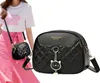 A person is modeling a small black quilted crossbody bag with a cat charm. Náhľad obrázku produktu