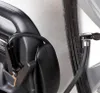 A close-up view of a car tire valve stem connected to a black hose, which is attached to a black device with a metal clamp. Podgląd zdjęcia produktu