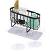A black wire rack for a sink, holding a spray bottle, a tube of cream, and a green sponge. It is attached to a grey pad with two clear adhesive hooks. Produktbild-Vorschau