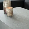 Two decorative candle holders with a textured, glittery finish are placed on a grey surface, possibly a table. The background is dark and out of focus, suggesting an indoor setting. Produktbild-Vorschau
