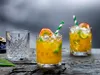Three glasses of tropical cocktails with passion fruit and lime garnishes, placed on a rustic wooden surface. Produktbild-Vorschau