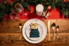 A Christmas-themed table setting with a festive runner, candles, and a place setting featuring a napkin folded like a Christmas tree. Produktbild-Vorschau