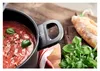A close-up of a pot of tomato soup with basil and a baguette in the background. Náhled obrázku produktu