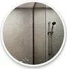 A round mirror with a white frame reflects a modern bathroom with gray tiled walls and a shower head. Produktbild-Vorschau