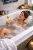 A woman relaxing in a bubble bath with a drink. Produktbild-Vorschau