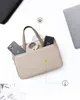 A beige laptop bag is shown with a smartphone, charging cable, and a power bank inside. A laptop is partially visible in the upper right corner. Produktbild-Vorschau