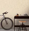 A bicycle is parked next to a desk with a stool in front of it. The wall behind them has a textured wallpaper. Produktbild-Vorschau