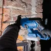 A person is using a blue and black cordless rotary hammer drill to drill into a brick wall. Produktbild-Vorschau