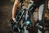 A person is holding the handlebars of a black electric bicycle with fat tires, outdoors on a dirt path. Produktbild-Vorschau