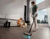 A man is vacuuming a living room while a woman sits on the couch petting their dog. Náhled obrázku produktu