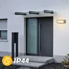 A modern house entrance with a glass canopy over the door, a wall light, and a mailbox, during a rain shower. Anteprima dell’immagine prodotto