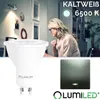 A woman is working at a desk in a room with artwork on the wall, while a product image of an LED bulb is shown in the foreground. Náhled obrázku produktu