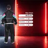 A person wearing a tracksuit stands in front of a brick wall with neon lights, next to a size chart. Anteprima dell’immagine prodotto