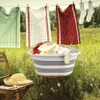A collapsible laundry basket filled with laundry is placed on a tree stump in a grassy outdoor setting, with clothes hanging on a line in the background. Anteprima dell’immagine prodotto