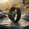 A smartwatch with a green heart rate sensor is placed on a rock, with running shoes and a coiled rope nearby. A person is running on a trail in the background. Náhled obrázku produktu