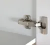 A close-up view of a cabinet hinge attached to a white cabinet door and frame. Podgląd zdjęcia produktu