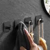 A hand is shown hanging a gray towel on a black hook mounted on a textured gray wall. Two other hooks are visible, one with a rope and wooden brush hanging from it. Anteprima dell’immagine prodotto
