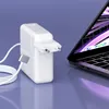 A white Apple MacBook charger and cable are placed next to a MacBook laptop on a purple surface. Produktbild-Vorschau