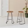 Two bar stools with wooden seats and black metal legs are placed on a white floor in front of a light beige wall. A white door is visible on the left, and a potted plant is on the right. Anteprima dell’immagine prodotto