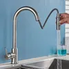 A hand is holding a pull-down kitchen faucet as water flows into a glass and a sink. Produktbild-Vorschau