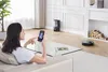 A woman is relaxing on a couch while controlling a robot vacuum cleaner with her smartphone. Produktbild-Vorschau