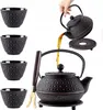 A hand pours tea from a cast iron teapot into a cup, with other cups and a tea strainer visible. Podgląd zdjęcia produktu