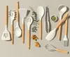 A collection of white silicone kitchen utensils with wooden handles laid out on a light gray surface. Náhled obrázku produktu