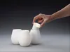 A hand is placing a light source into a white ceramic candle holder. Produktbild-Vorschau
