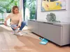 A woman is cleaning the floor under a cabinet with a mop. Anteprima dell’immagine prodotto