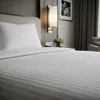 A close-up view of a neatly made hotel bed with white striped bedding. Produktbild-Vorschau