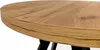 A close-up view of the edge of a round wooden table with black legs visible underneath. Produktbild-Vorschau