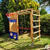 A wooden playground structure with a basketball hoop, climbing net, and swings, set in a grassy backyard with trees and bushes. Voir les images du produit