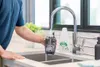 A person is filling a cleaning solution tank under a kitchen faucet. Voir les images du produit
