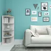 A white corner shelf unit filled with books and decorative items, placed next to a white sofa in a room with turquoise walls. Produktbild-Vorschau