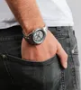 A close-up shot of a man's wrist wearing a silver watch, with his hand in the pocket of his dark jeans. Anteprima dell’immagine prodotto