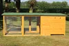 A wooden chicken coop with a green roof is set up on a grassy lawn, with trees and foliage in the background. Produktbild-Vorschau
