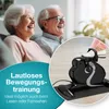 An elderly couple is sitting on a couch and smiling, while a mini exercise bike is shown in the foreground. Produktbild-Vorschau