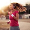 A woman is running outdoors with headphones on, with the sun setting behind her. Produktbild-Vorschau