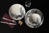 A table setting with plates, a bowl, cutlery, a napkin, and a glass of water, arranged on a dark surface. Anteprima dell’immagine prodotto