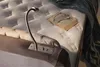 A close-up view of a bed with a book and glasses on the mattress, and a reading lamp attached to the headboard. Produktbild-Vorschau