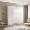 A modern bedroom with a large white high-gloss wardrobe, a stylish armchair, a floor lamp, and a coffee table with a rug. Produktbild-Vorschau