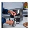 A person is using a silver espresso machine in a kitchen. Produktbild-Vorschau