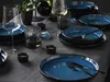 A table setting with blue stoneware plates, glasses, and candles. Produktbild-Vorschau
