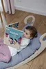A young child is lying on a Montessori rocking cushion and reading a book. Produktbild-Vorschau