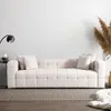 A beige bouclé sofa is shown in a minimalist living room setting with a floor lamp and dried grass accents. Voir les images du produit