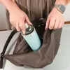 A person is placing a water bottle into a brown leather handbag. Anteprima dell’immagine prodotto
