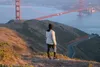 A person stands on a hill overlooking the Golden Gate Bridge, holding a water bottle. Podgląd zdjęcia produktu