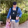 A father is carrying his baby in a carrier, with his older daughter standing next to him. Produktbild-Vorschau